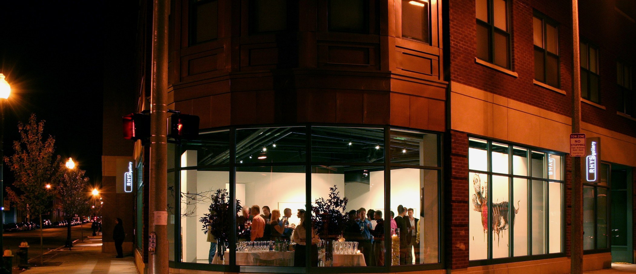 RHYS Gallery at night — lit sign and opening visible through the windows